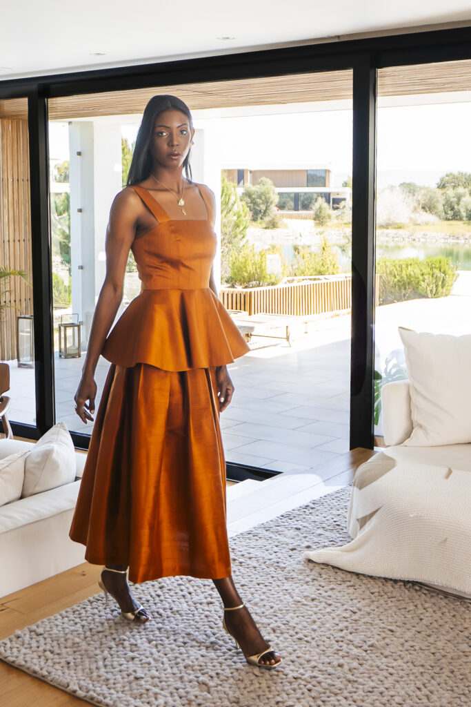 A Decade of Design: Roselyn Silva on Intentional Elegance and Her São Tomé Roots 5 A model in a rust tiered dress standing in a bright room open to a garden