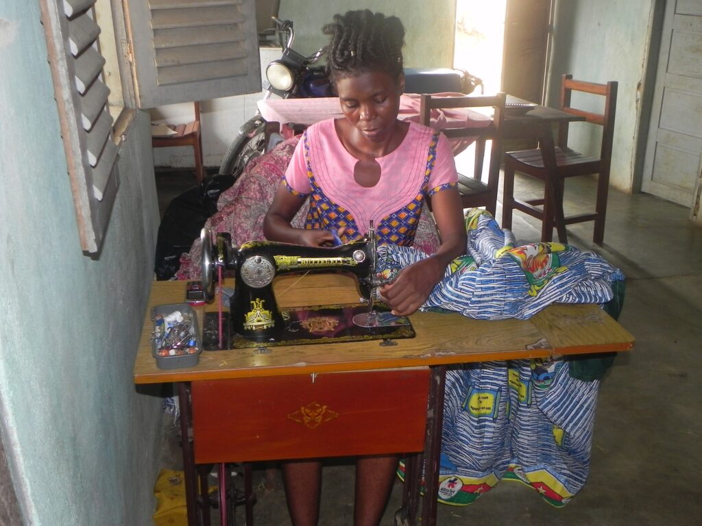 A Tanzanian seamstress sits at her sewing machine, stitching brightly colored fabric in her workshop.