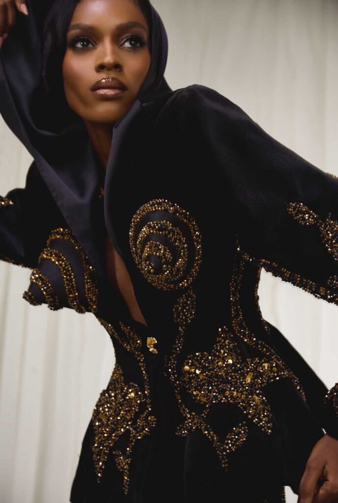 A model wears a dramatic black hooded gown by SEVON Dejana, embellished with intricate gold beading and sequins. The garment, styled by The Style Pundit for A Devil Is A Liar, embodies Nollywood’s new era of luxury fashion on screen.