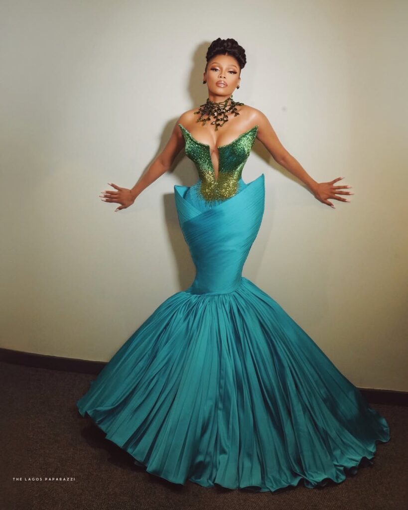 Bonang Matheba poses in a dramatic teal and green corseted gown by Veekee James, styled by Dahmola, against a neutral backdrop.