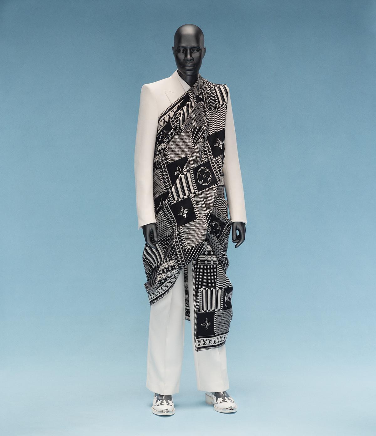 A mannequin dressed in a sleek white suit and patterned black and white fabric wrap stands against a soft blue background, exuding elegance and modernity.