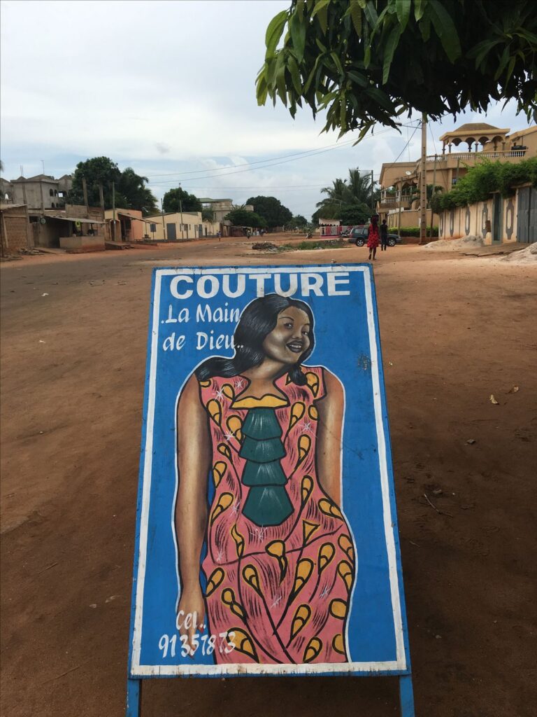 Hand-painted sign for a tailoring shop in Togo reading “Couture La Main de Dieu.”