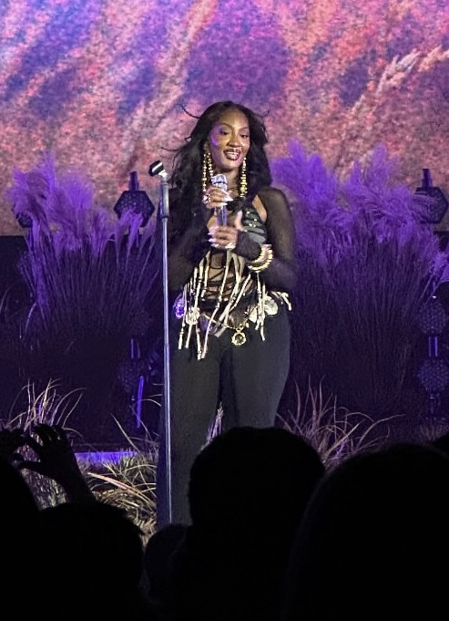 Nigerian singer Tems in concert in 2025, wearing a sleek stage outfit and singing passionately into a microphone.