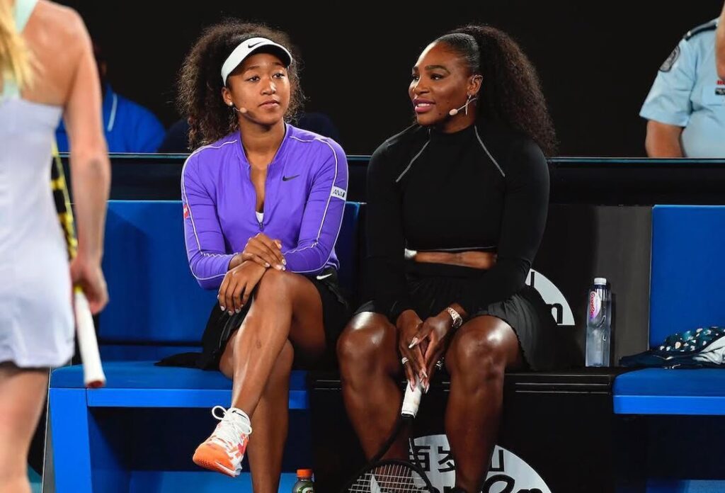 Naomi Osaka and Serena Williams sitting side by side during a U.S. Open match, wearing purple and black outfits.
