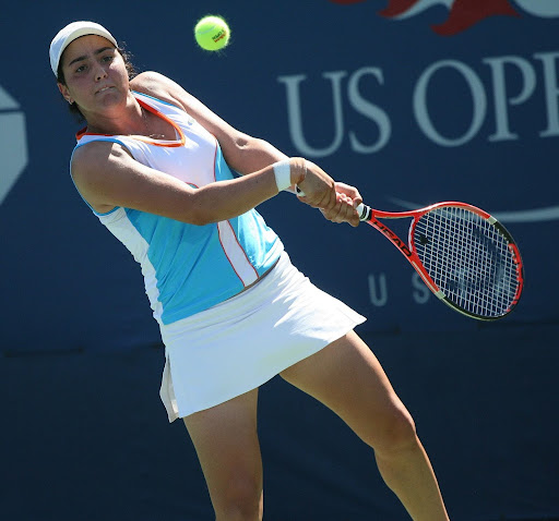 Ons Jabeur preparing to hit a forehand at the U.S. Open, wearing a white visor and match kit.