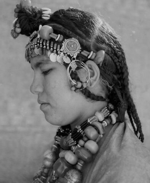 Black-and-white portrait of an Amazigh woman from Morocco wearing braids and ornate jewelry made of amber, coral, and silver.