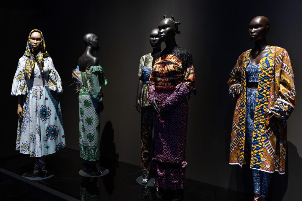 Africa Fashion Arrives in Montreal: A Global Conversation Continues 5 Contemporary looks combining printed cottons and wax fabrics from various African designers against a dark backdrop.