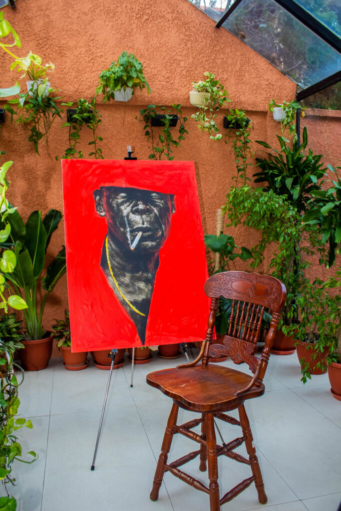 Anthony Azekwoh's Red Man hung on a terracotta wall beside plants and a wooden stool