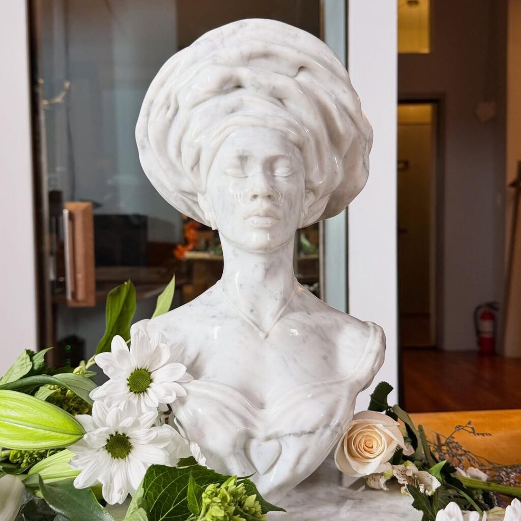 Tolani by Anthony Azekwoh, a white bust wearing a sculpted headwrap, displayed beside white flowers