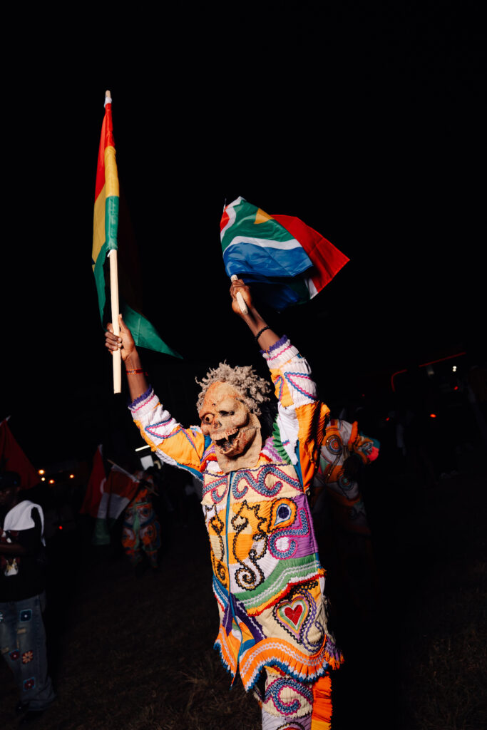 A reveller in a brightly patterned outfit holding a flag aloft in a crowd