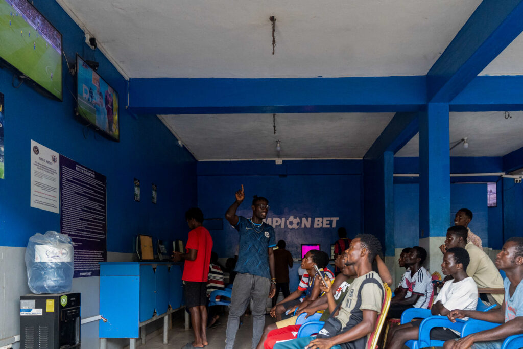 Young men seated inside a blue-painted betting shop watching screens