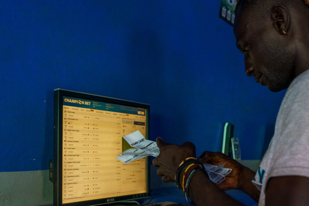 A man leans over a screen of betting odds while handling cash at a shop counter