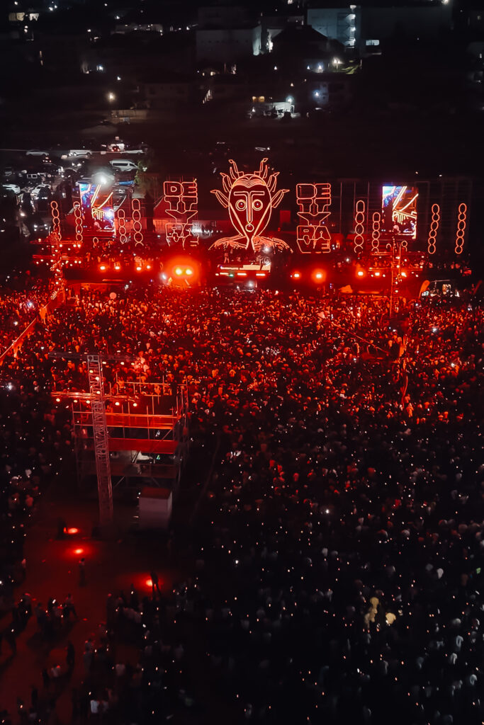 Aerial view of a dense crowd lit red at an outdoor night event in Accra