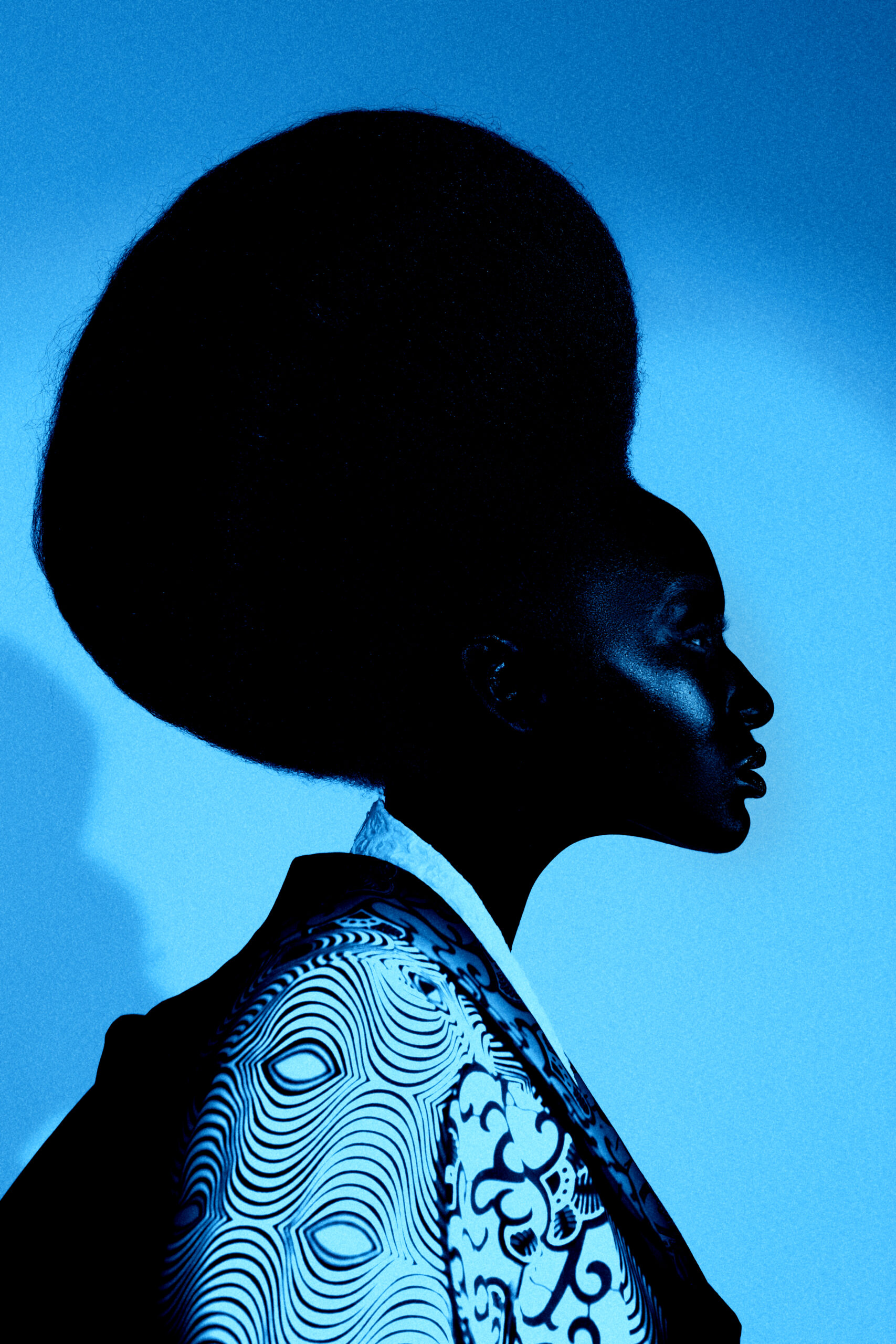 Profile silhouette of a model in a graphic print jacket against a deep blue background, from the Umunwanyi Town Council collection by Ohlanna Bu Zikora.