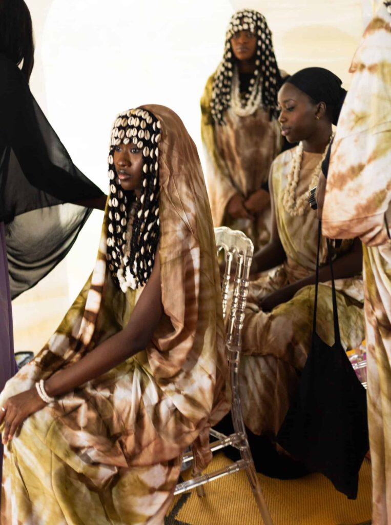 A group of models wearing avant-garde West African fashion featuring voluminous cowrie shell headpieces and woven textiles, representing the evolution of African cultural heritage into global luxury capital.