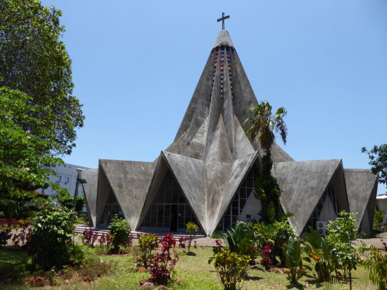 Folded concrete church with angular roof forms against blue sky. Igreja de Santo António de Polana, modernist architecture in Maputo, Mozambique, designed by Nuno Craveiro Lopes, 1962.