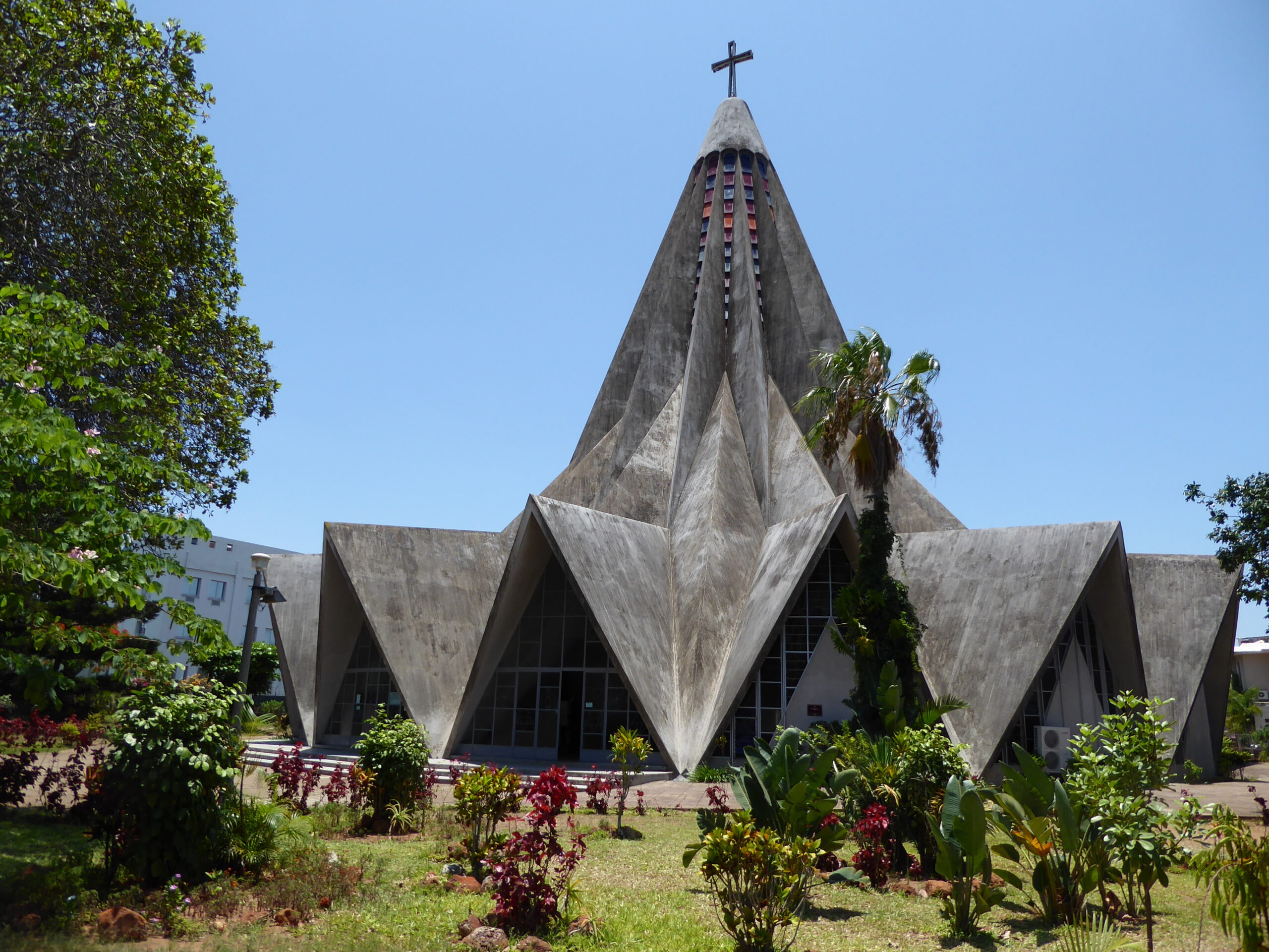 Folded concrete church with angular roof forms against blue sky. Igreja de Santo António de Polana, modernist architecture in Maputo, Mozambique, designed by Nuno Craveiro Lopes, 1962.