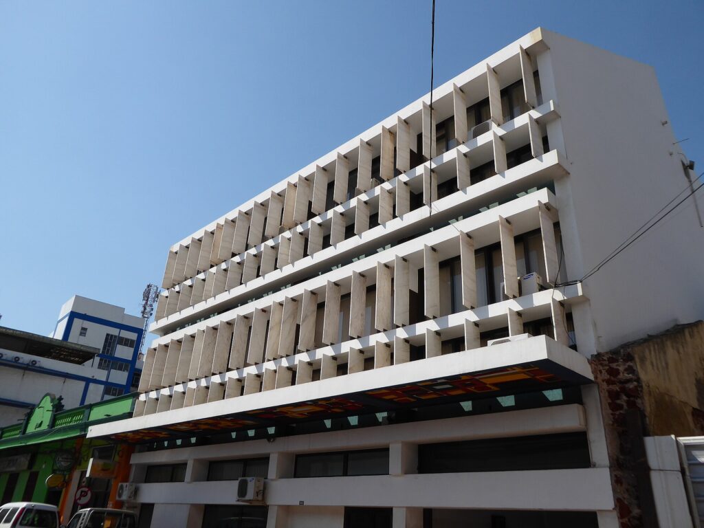 Modernist apartment building with deep horizontal brise-soleil facade casting rhythmic shadows. Prédio Mann George by Pancho Guedes, Maputo, Mozambique.