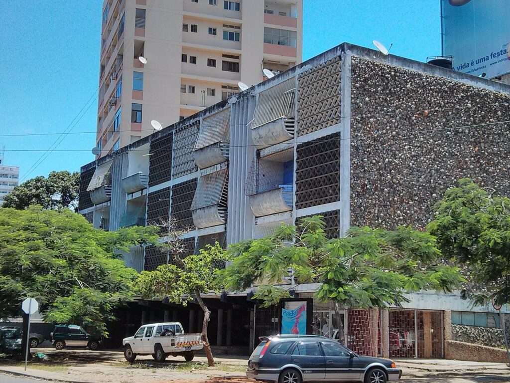 Brutalist apartment building on pilotis with triangular concrete lattice screen, curved canopies, and pebble-aggregate wall. Edifício Dragão by Pancho Guedes, 1951, Maputo, Mozambique.