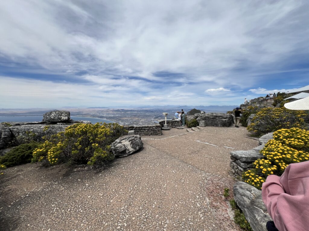 The Best Places to Propose in Africa: From Cape Town to Marrakech 2 Panoramic view from the top of Table Mountain in Cape Town, showing a rocky path overlooking the city, coastline, and the Atlantic Ocean under a clear sky.