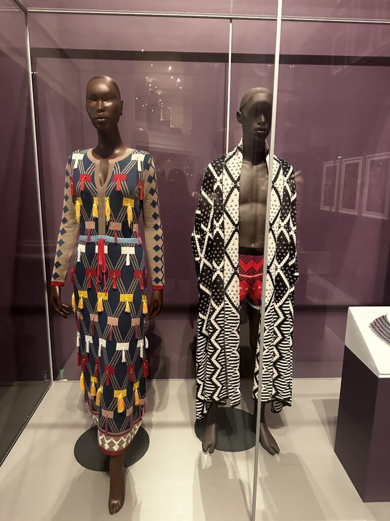 Installation view of MaXhosa Africa knitwear designs on mannequins at the Brooklyn Museum Africa Fashion exhibition, showcasing modern luxury clothing featuring traditional Xhosa-inspired geometric patterns.
