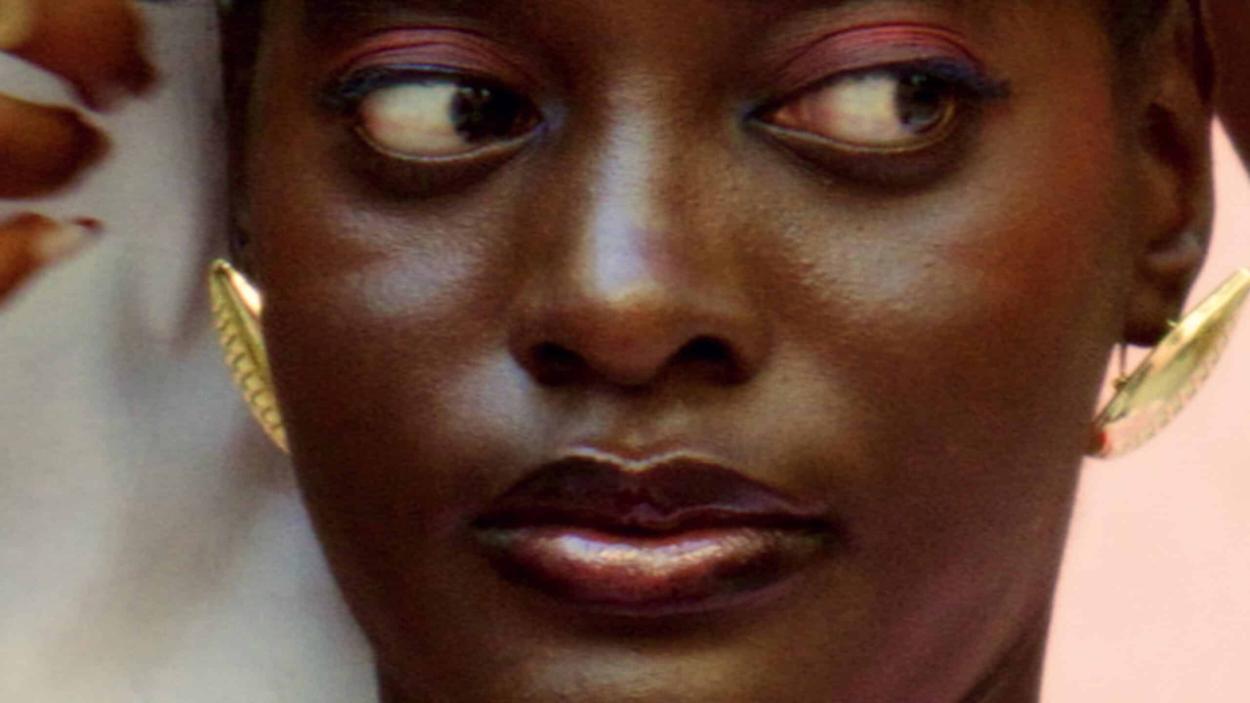 A film still from Ntfufi ya Ntaba by Aton Ntsiba, showing a close-up portrait with gold earrings against a soft background.