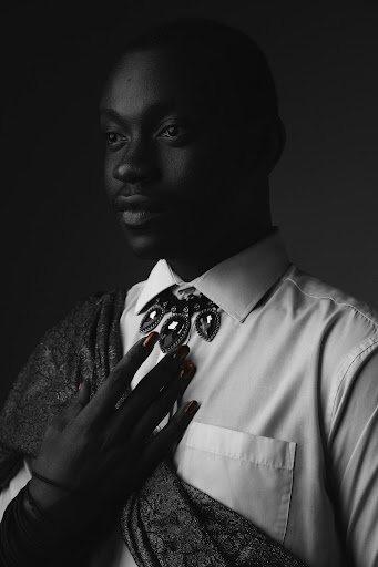 Black and white portrait of designer Zikora in a shirt and bow tie with gloved hands
