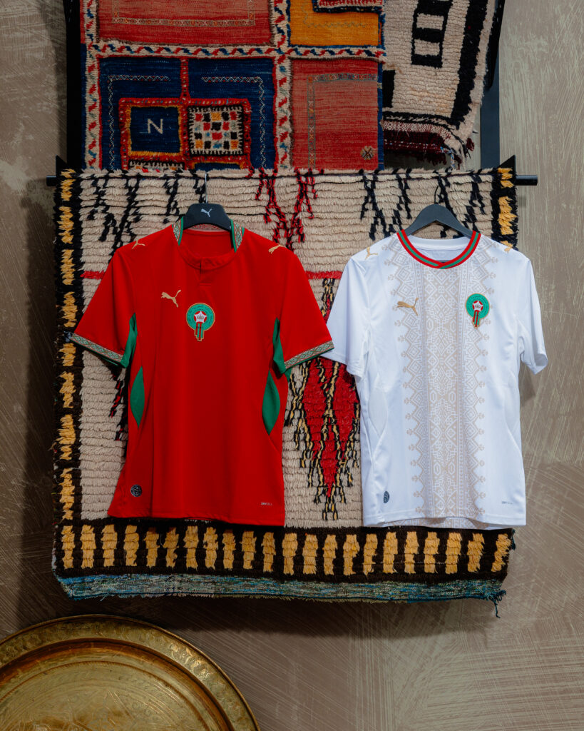 The red home and white away PUMA Morocco 2026 World Cup jerseys hanging side-by-side on a wooden rack.