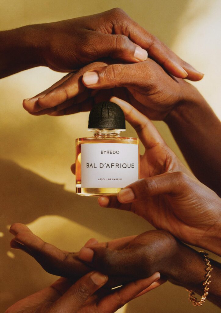 Multiple hands cradling Byredo Bal d'Afrique Absolu de Parfum bottle in golden light, photographed by Philip-Daniel Ducasse