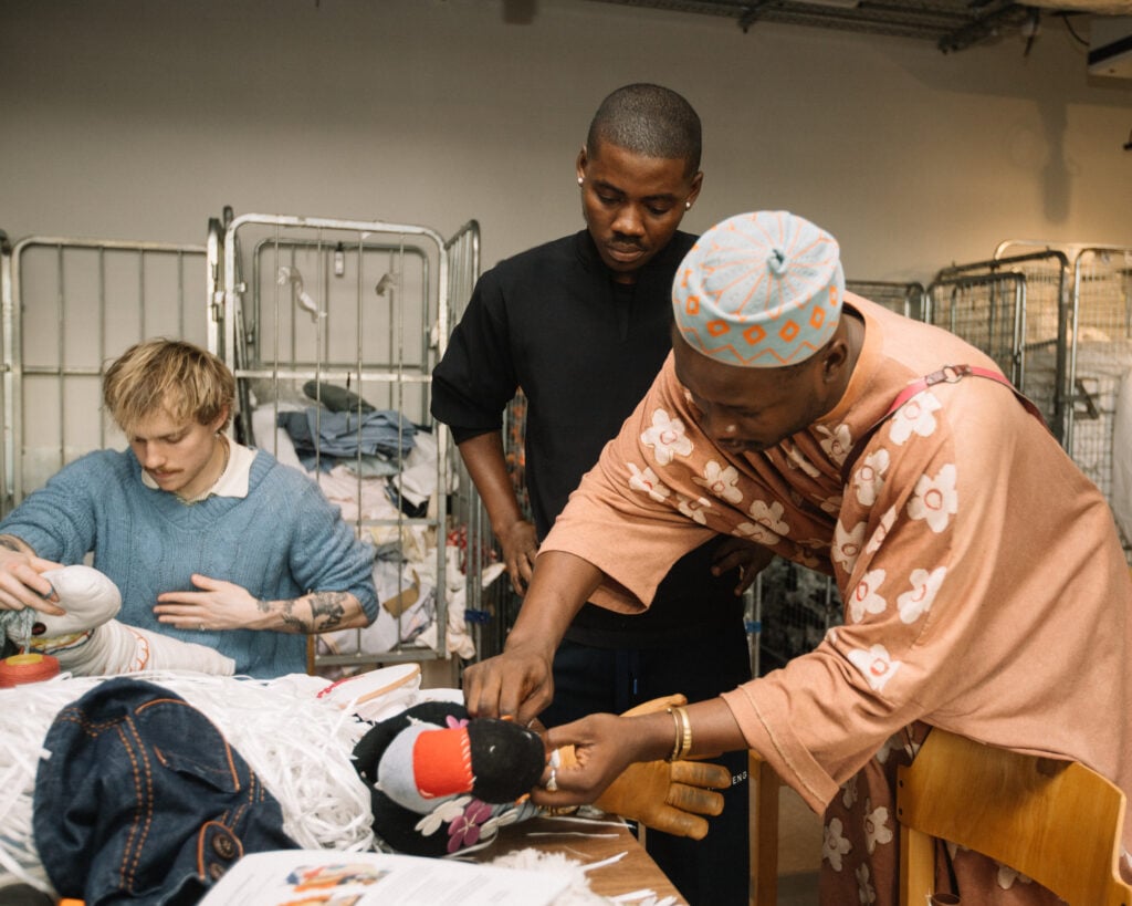 Inside Central Saint Martins’ Makers Camp: West African Makers in Focus 2 Designers Peter Acha and Travis Obeng-Casper collaborating on a textile project at the Central Saint Martins Makers Camp, using hand tools to manipulate fabric on a workbench.