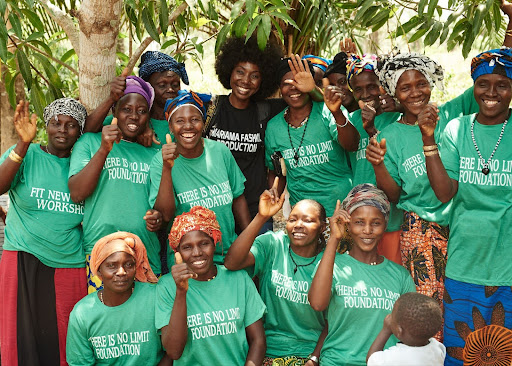 Material Literacy: The Knowledge in Cloth 7 A large group of smiling women artisan tie-dyers, many wearing matching green shirts, gathered outdoors with Mariama Camara during a 2019 natural dye workshop in Kindia, Guinea.
