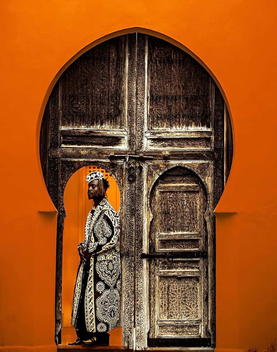 Fahd Al Marsaoui wearing an embroidered black and white kaftan standing in an orange Moorish archway in Marrakech