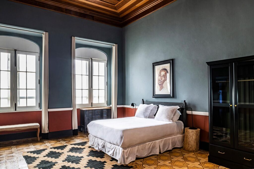 Bedroom at Cacao House with local portrait artwork, patterned tile floor, and arched colonial windows at Roça Sundy 