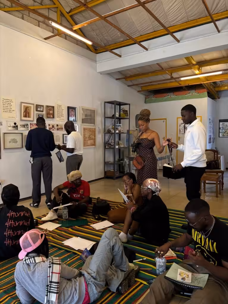 Workshop participants sitting on a striped mat with sketchbooks while others view framed photographs on a gallery wall