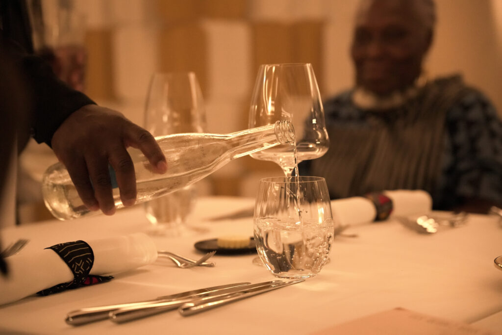 Kondokpo: Georgiana Viou and Nokx Majozi at Sofitel Cotonou 8 A server pouring water into a glass at an elegantly set table during the Kondokpo culinary event at Sofitel Cotonou.