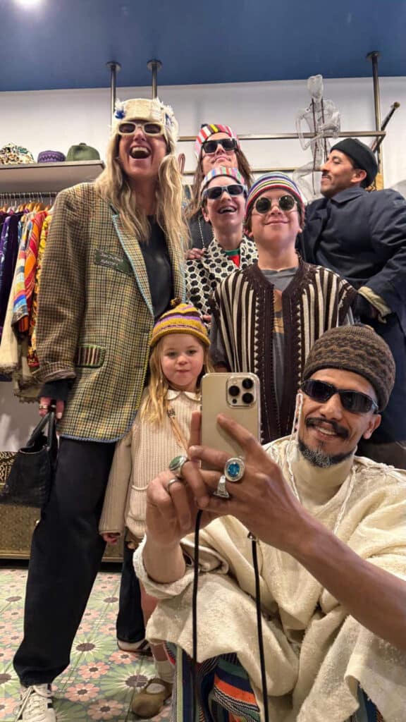 Fahd Al Marsaoui takes a mirror selfie with customers and their children all wearing vintage hats and styled pieces inside Funky Cool Medina store in Marrakech
