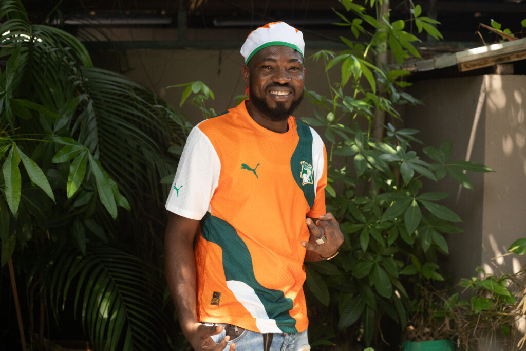 A football fan smiling while wearing a Côte d'Ivoire Puma replica jersey outdoors.