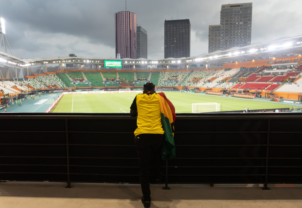 The Jersey Economy: Why Africa Is the Most Valuable Untapped Market in Sports Merchandise 2 Football fans wearing yellow jerseys standing in the stadium stands overlooking the field.
