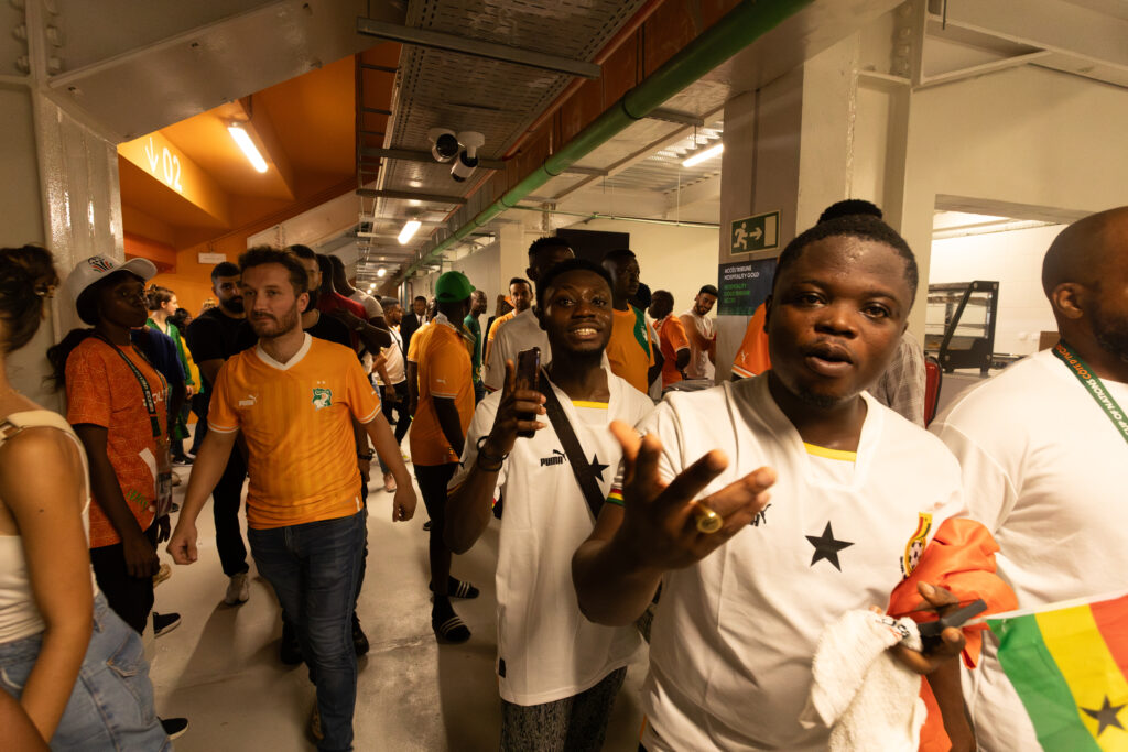 The Jersey Economy: Why Africa Is the Most Valuable Untapped Market in Sports Merchandise 7 African football fans in orange replica jerseys gathering at an indoor venue, with one man smiling and gesturing at the camera.