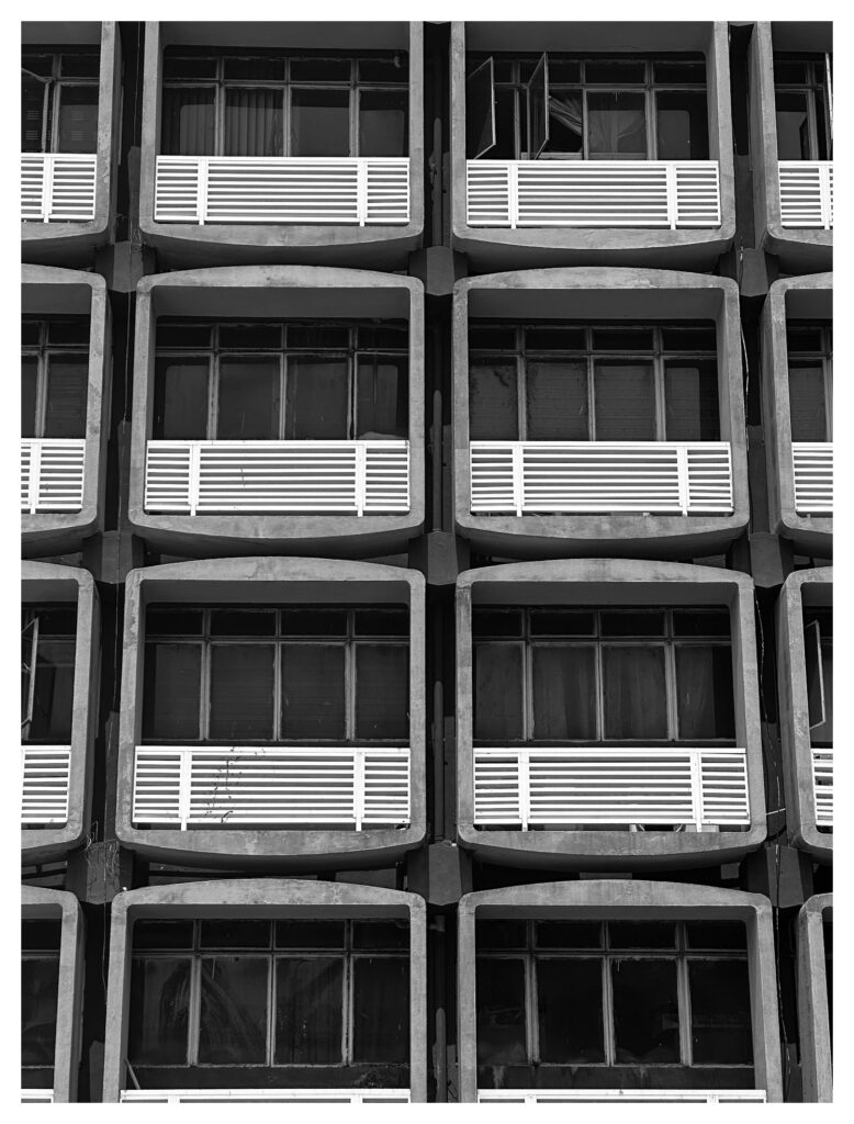 Angled perspective of rounded concrete window bays receding along a brutalist facade at the University of Lagos, with a sweeping concrete overhang slicing across the sky.