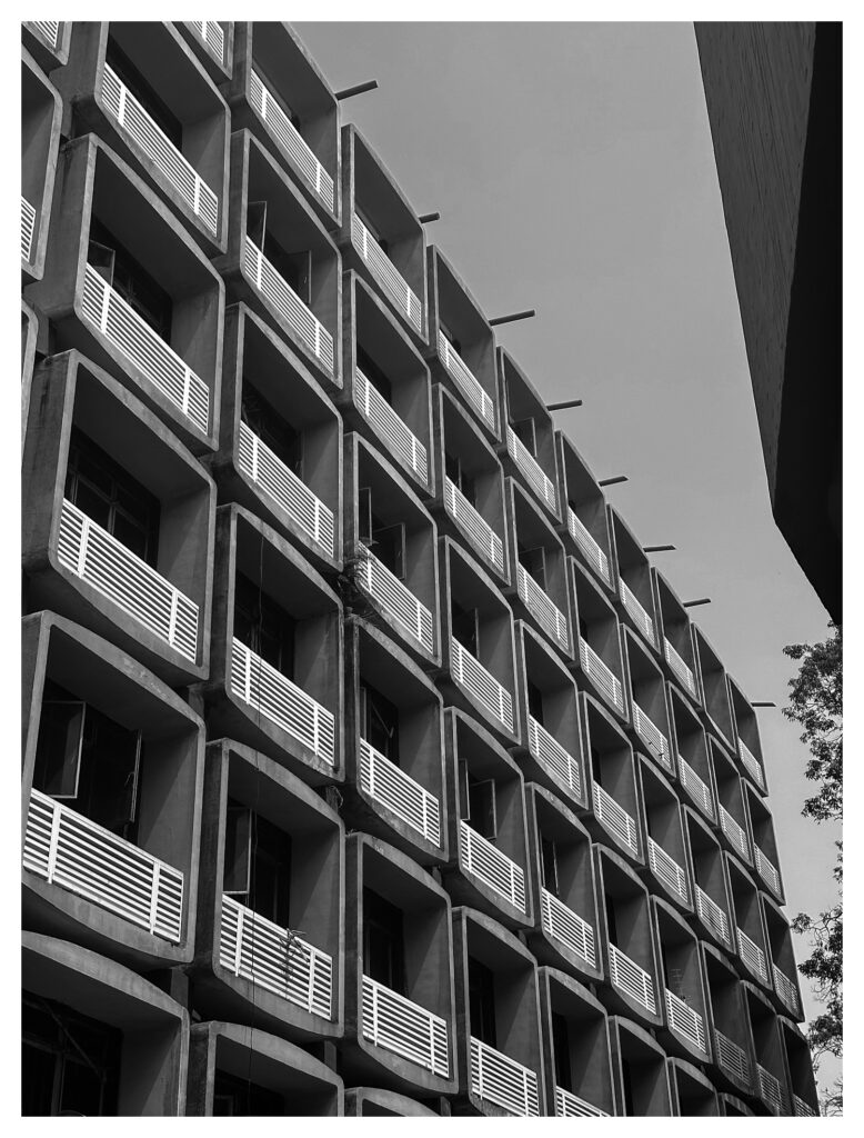 Frontal view of a repeating grid of rounded concrete window bays with horizontal louver shutters on a brutalist building at the University of Lagos.