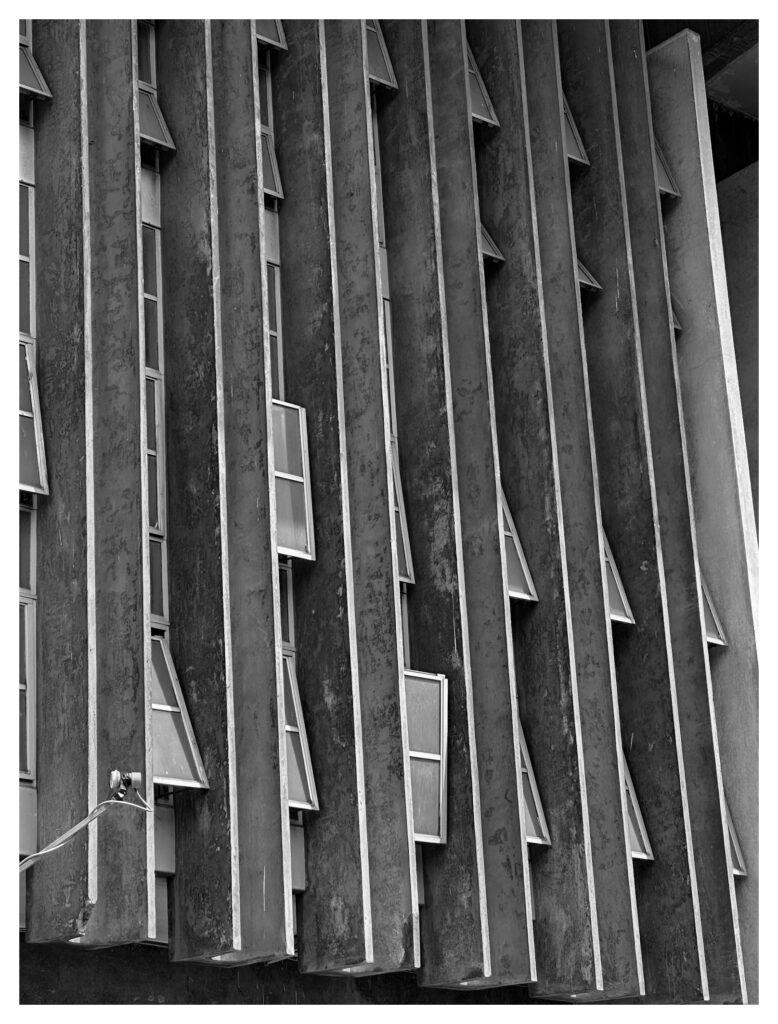 Rows of tall vertical concrete fins with small awning windows on a brutalist building facade at the University of Lagos, photographed in black and white.