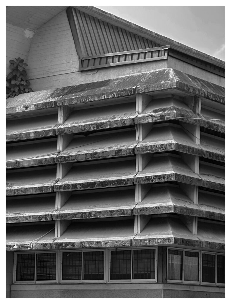 Horizontal concrete louvers and a peaked roofline on a post-colonial modernist building at the University of Lagos, with ground-floor windows visible below.