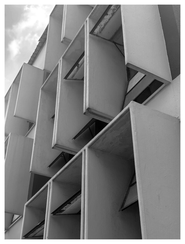 Diagonal view of projecting concrete sun breaker boxes on a modernist university building in Lagos, creating a geometric grid of light and shadow.