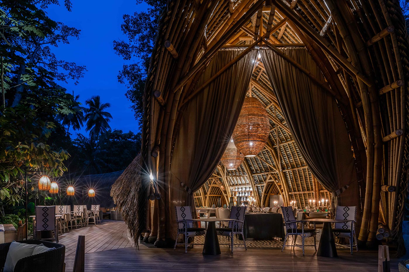 Open-air bamboo restaurant with handwoven pendant lights at Sundy Praia, Príncipe Island Meta description: Sundy Praia restaurant at dusk. Bamboo structure, handwoven lights, forest canopy.