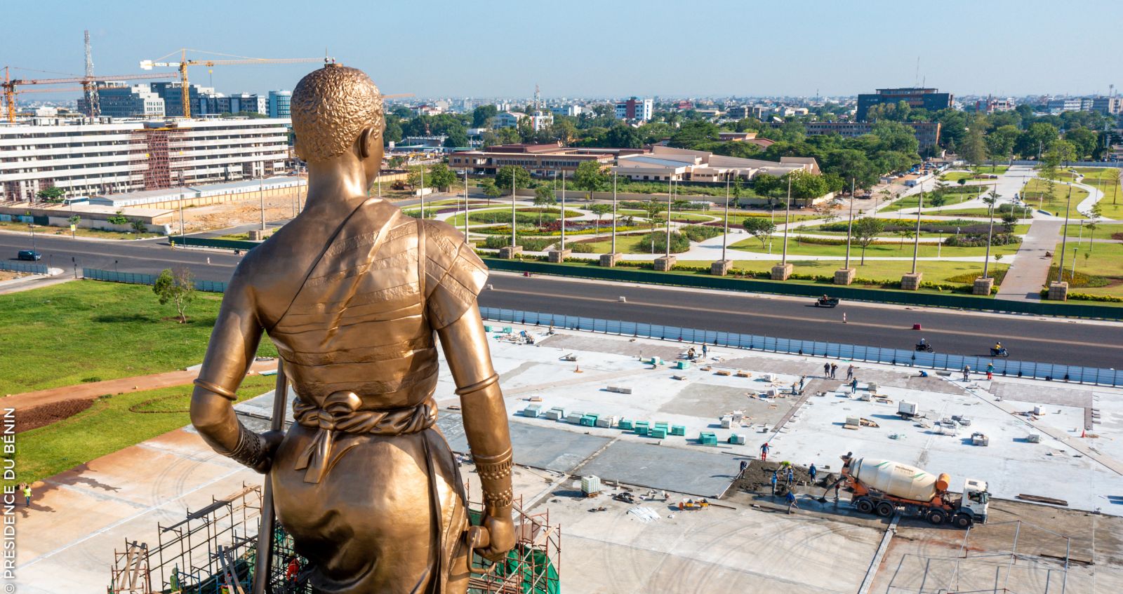 Bronze Amazone statue seen from behind overlooking construction and city infrastructure in Cotonou, Benin.