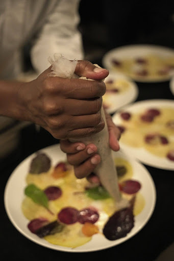 Kondokpo: Georgiana Viou and Nokx Majozi at Sofitel Cotonou 3 A chef adding final touches of niébé hummus to a carpaccio de betteraves dish during the Kondokpo culinary event.