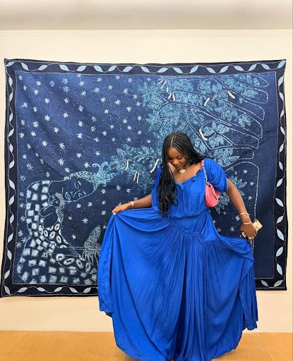 Woven Stories: 9 African Artists Shaping Contemporary Narratives Through Textiles 4 Nigerian artist Fadekemi Ogunsanya standing before her hand-embroidered Adire textile from the 'A miracle is a reasonable thing to ask for' exhibition, highlighting contemporary African material storytelling.