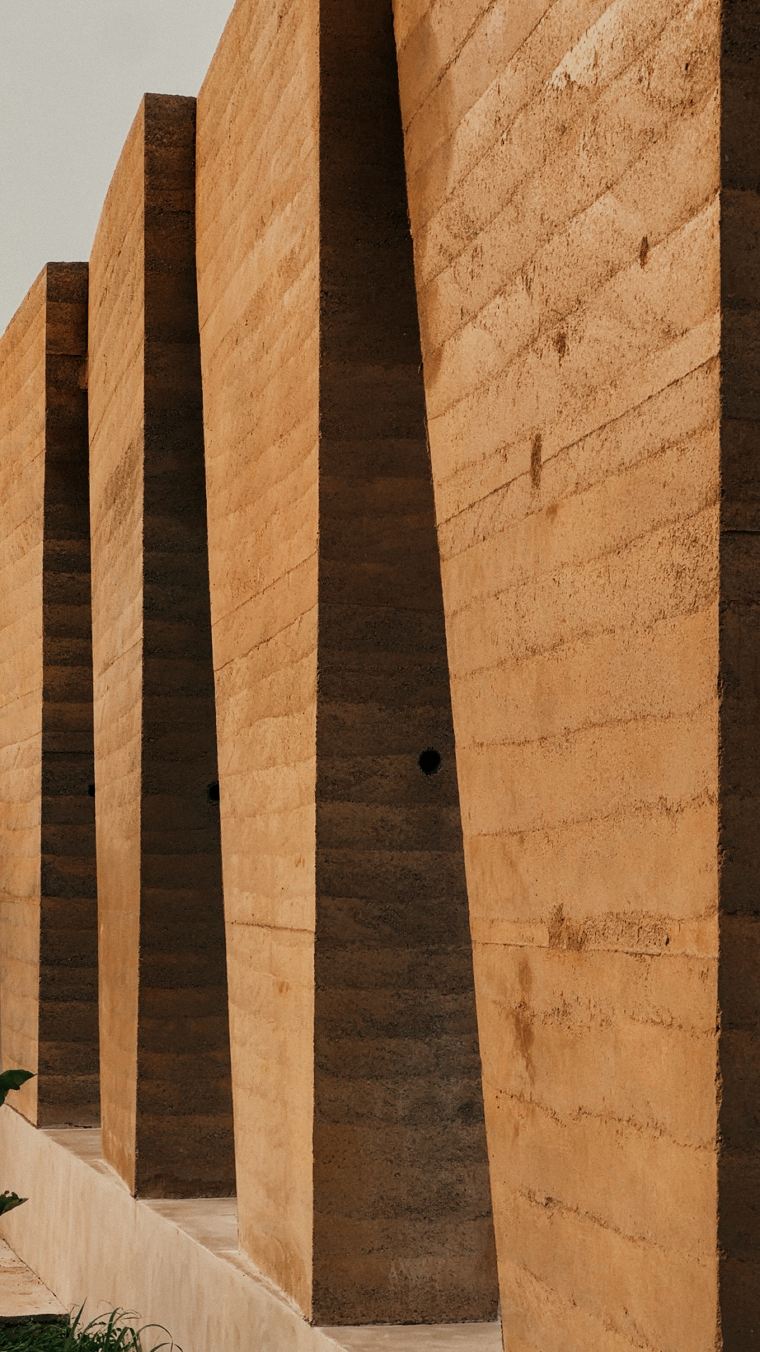 Thirty-three wedge-shaped rammed-earth panels installed at Backyard Community Club, Accra