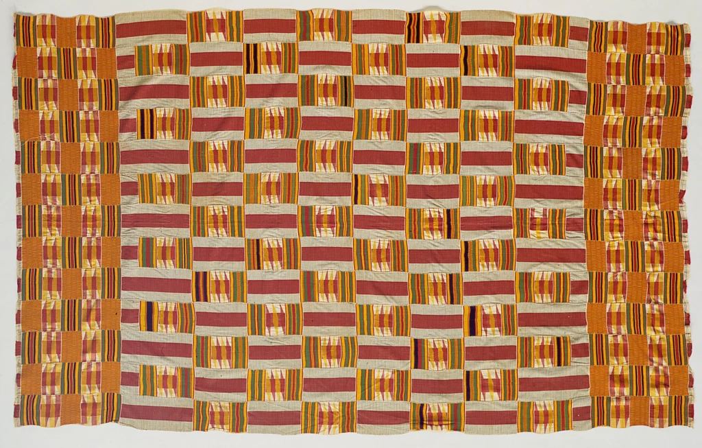 Kente and the Politics of Being Read 2 Asante kente cloth in red, gold, green, and cream blocks, woven strips sewn edge to edge, laid flat.